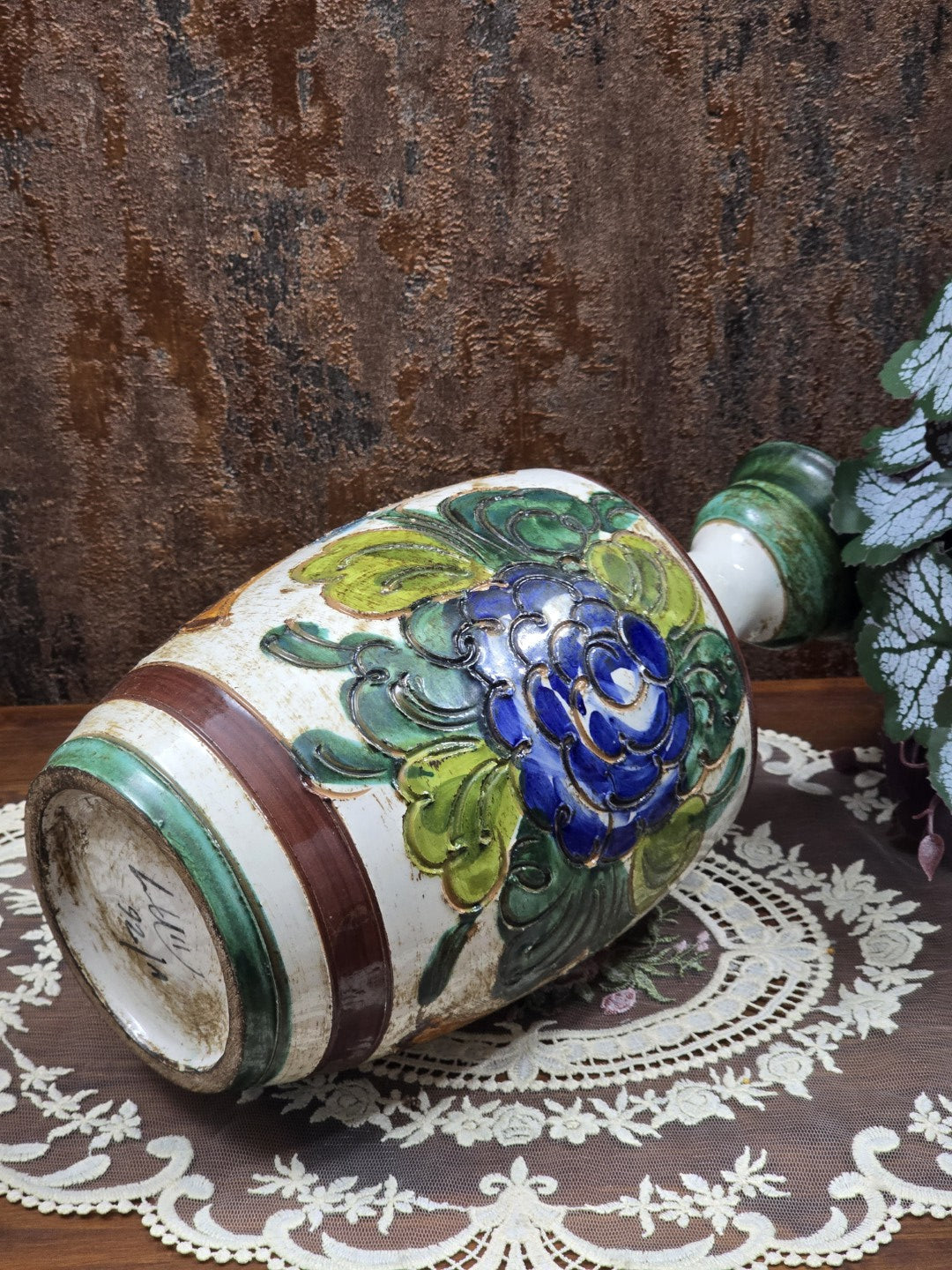 Keramikvase liegend mit blauem Blumendekor, grünen Blättern und sichtbarer Bodenansicht auf Spitzendecke