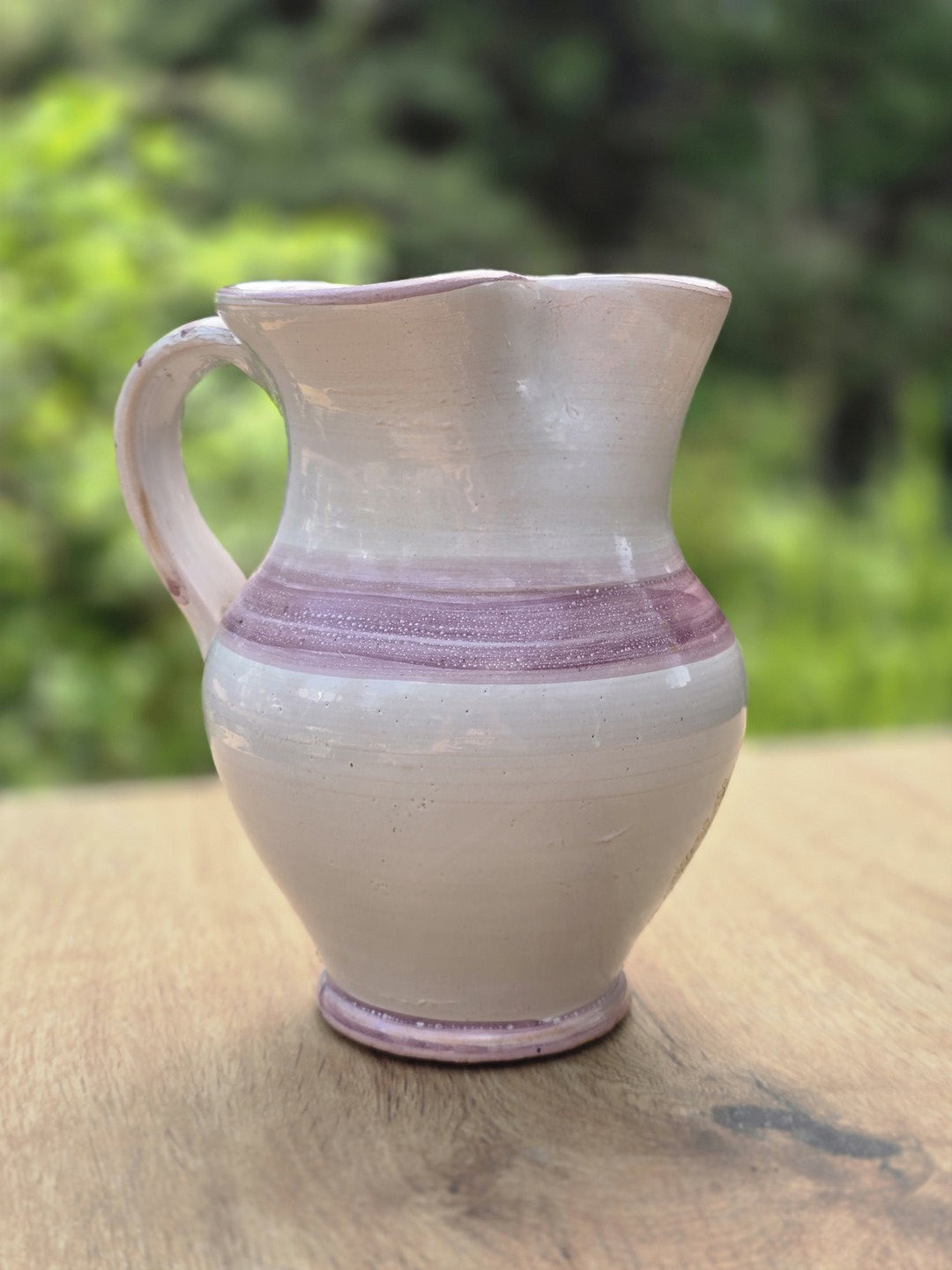 Seitliche Ansicht des Studiokeramik Krugs mit hellem Scherben, violettem Streifenmuster und handgeformtem Henkel.
