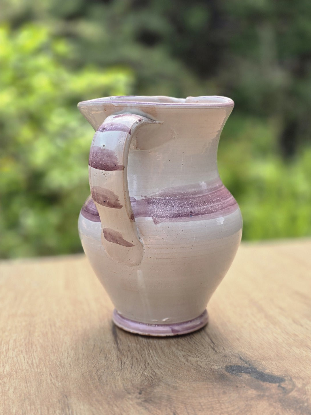 Rückseite eines bauchigen Vintage Keramikkrugs mit cremefarbener Glasur, violettem Dekorband und Henkel.