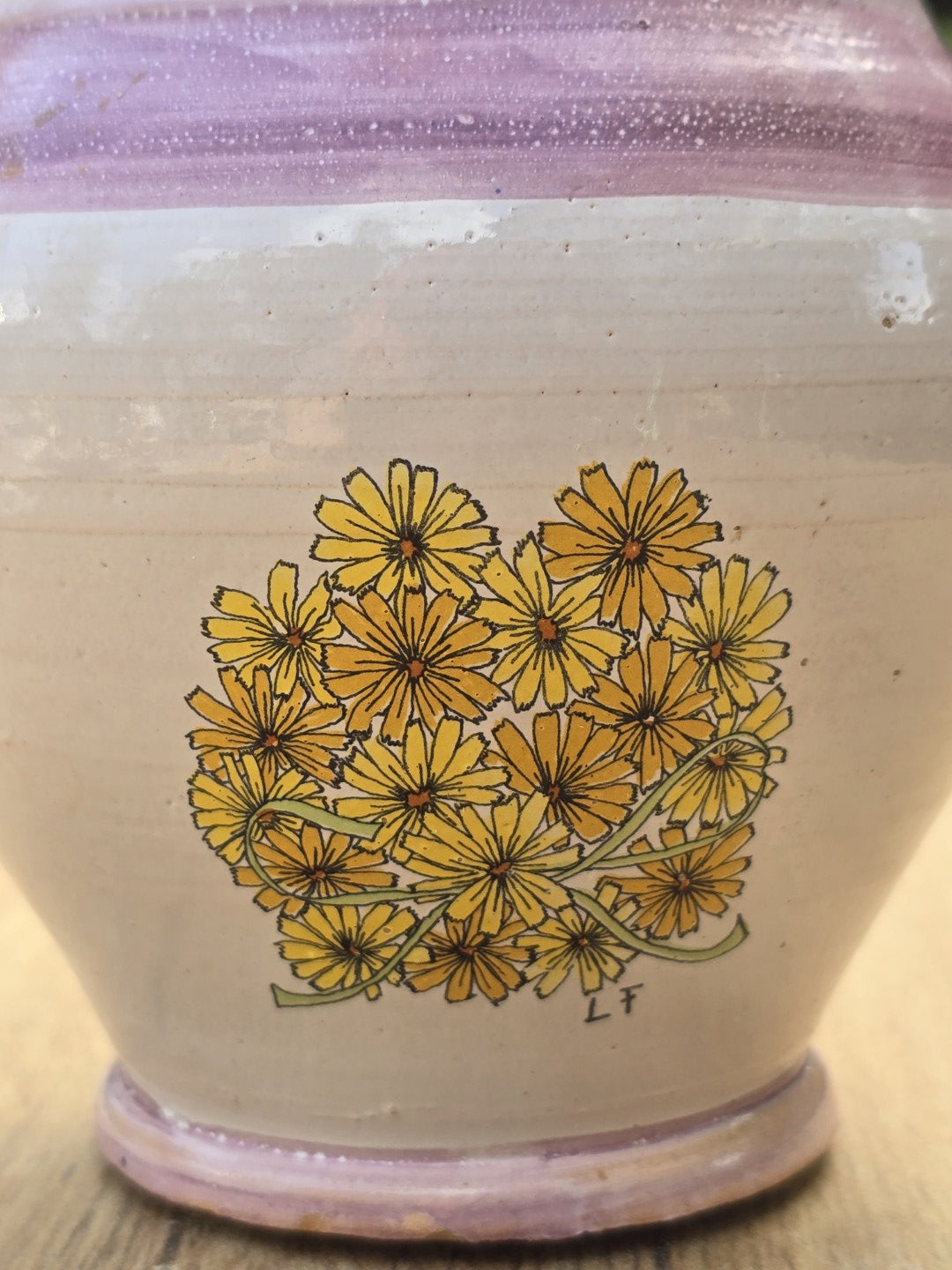 Nahaufnahme des gelben Blumendekors mit schwarzer Kontur und Signatur LF auf cremefarbener Keramik.