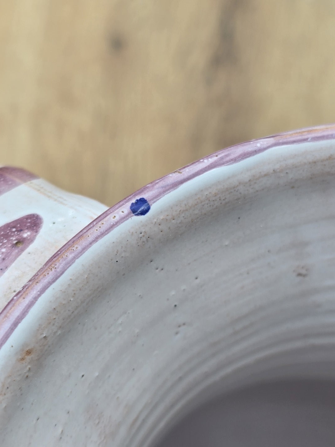 Detailaufnahme eines kleinen blauen Farbflecks am Rand des cremeweißen Keramikkrugs mit violettem Dekor.