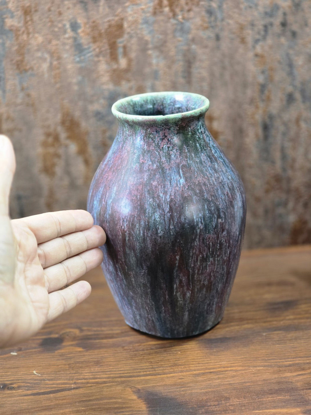 Vintage Studiokeramik-Vase mit changierender Laufglasur und bauchiger Form neben einer Hand zur Darstellung der Größe.