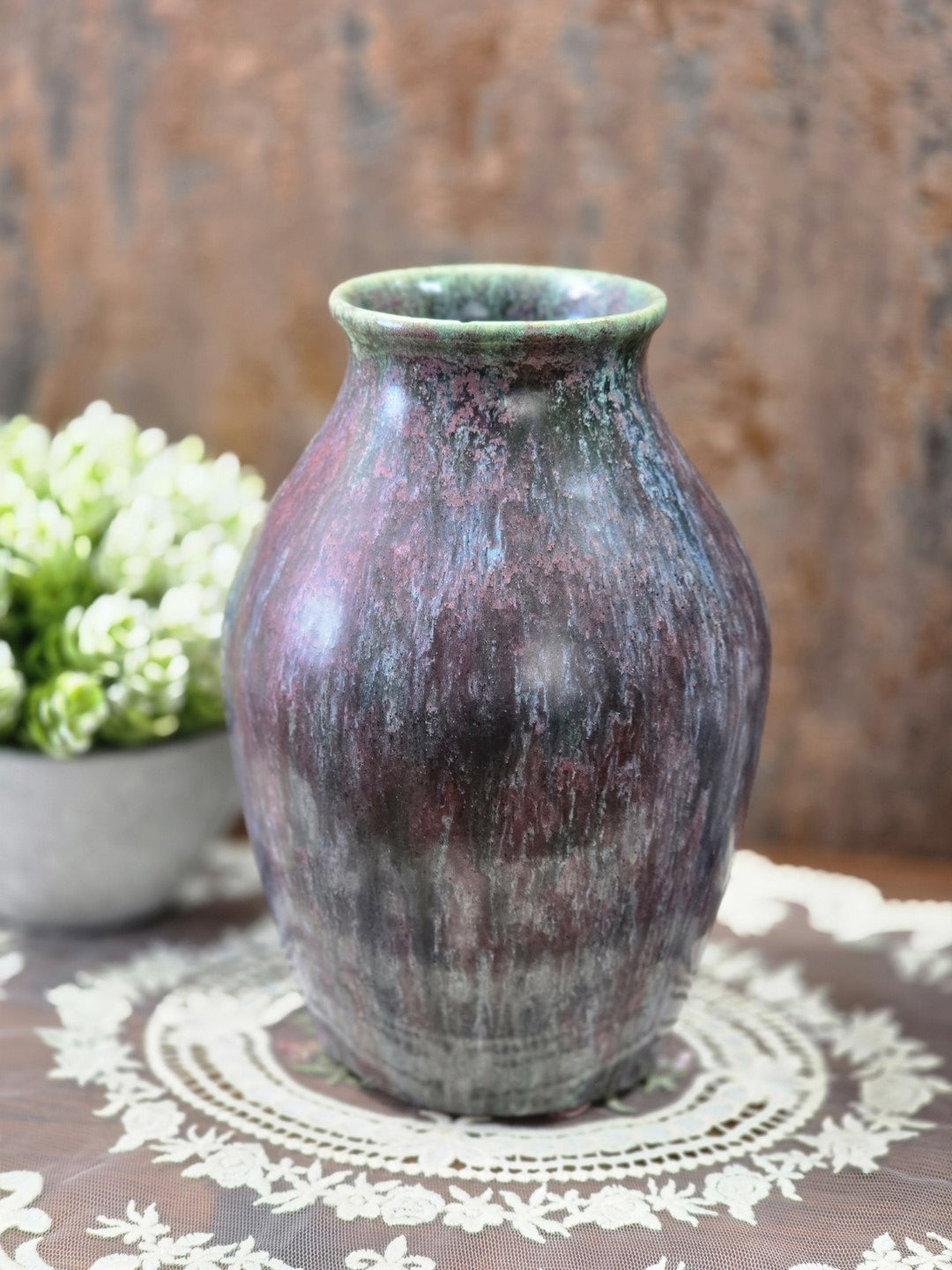 Vintage Studiokeramik-Vase mit bauchiger Form und changierender Glasur in Grün, Violett und Blau auf einer Spitzendecke.
