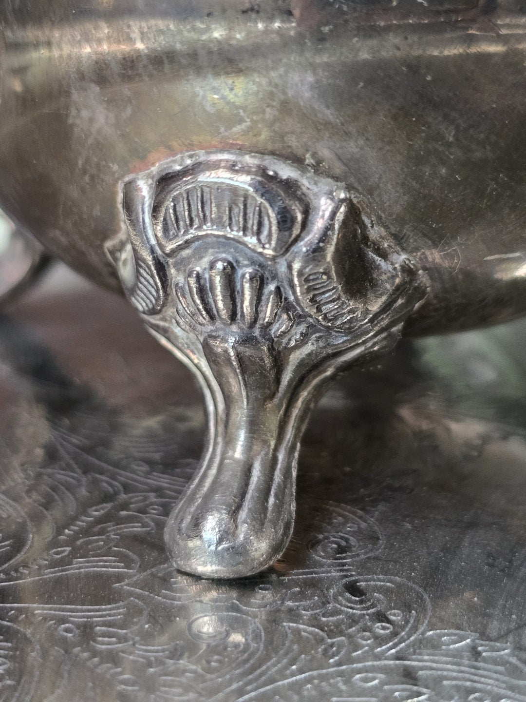 Teeservice-Fuß versilbert mit Muscheldekor, Patina und Kratzern auf graviertem Metalltablett in Detailansicht