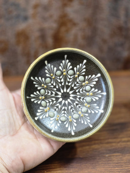 Vintage Keramikteller mit sternförmig angeordnetem Dekor und erhabenen grau-gelben Punkten, in der Hand gehalten