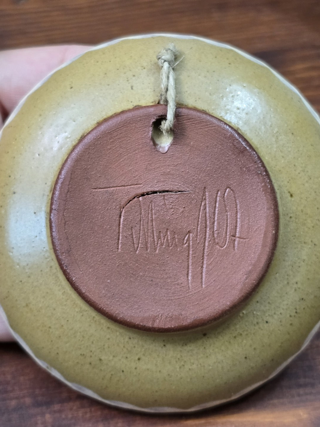 Vintage Keramikteller in Bodenansicht mit eingeritzter Signatur auf rötlichem Ton und sichtbarer Aufhängeschnur