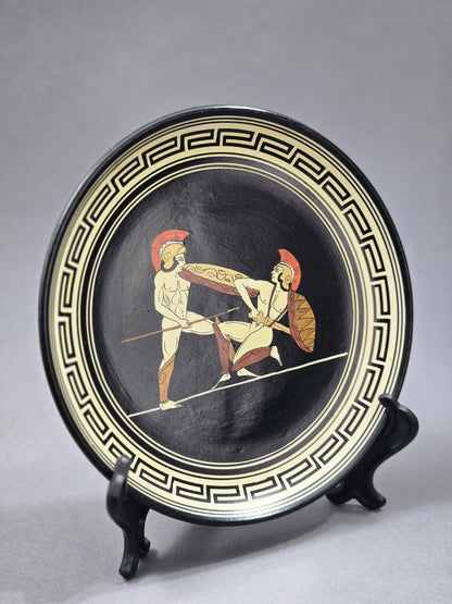 Vintage Wandteller mit griechischer Kampfszene in Creme, Rot und Ocker auf schwarzem Grund, schräg von links fotografiert