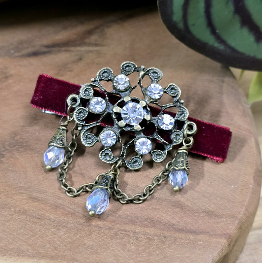 Das Bild zeigt eine Krokodilspange im Vintagelook mit Strass und dunkelrotem Samt, Kristallglasanhänger, Kettchen, Einzelstück

Lass dich von der zeitlosen Eleganz vergangener Epochen verzaubern mit dieser exquisiten Krokodilspange im Vintagestil. Sie ist kunstvoll verziert mit einem filigranen, antik bronzefarbigen Schmuckteil, welches mit funkelndem Strass besetzt ist. 
