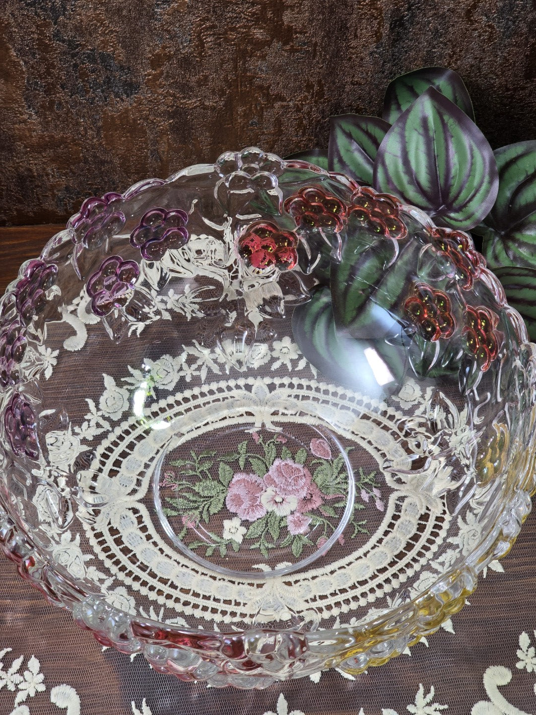 Klare Glasschale mit farbigem Blumenrelief, rundem Boden und sichtbarem Spitzendeckenmuster von oben fotografiert