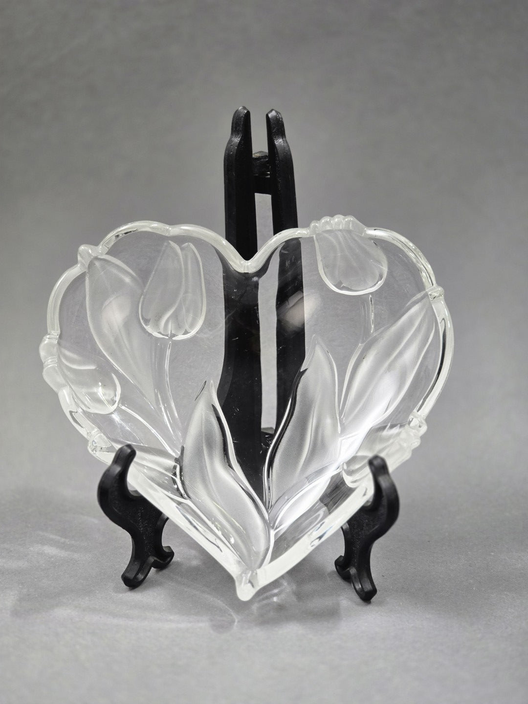 Vintage Walther Glasschale in Herzform mit Tulpen- und Blattrelief aus klarem Glas, frontal auf schwarzem Tellerständer gezeigt