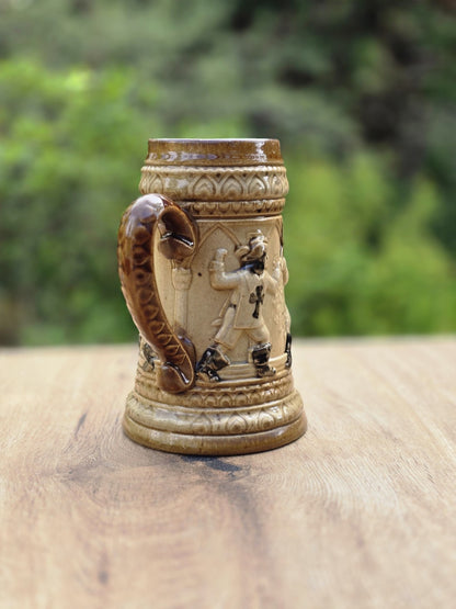 Braun-beiges Westerwald Bierseidel mit Landsknecht Relief, Tatzenkreuz auf der Brust, geschwungenem Henkel und kleiner Chipstelle am Standring.