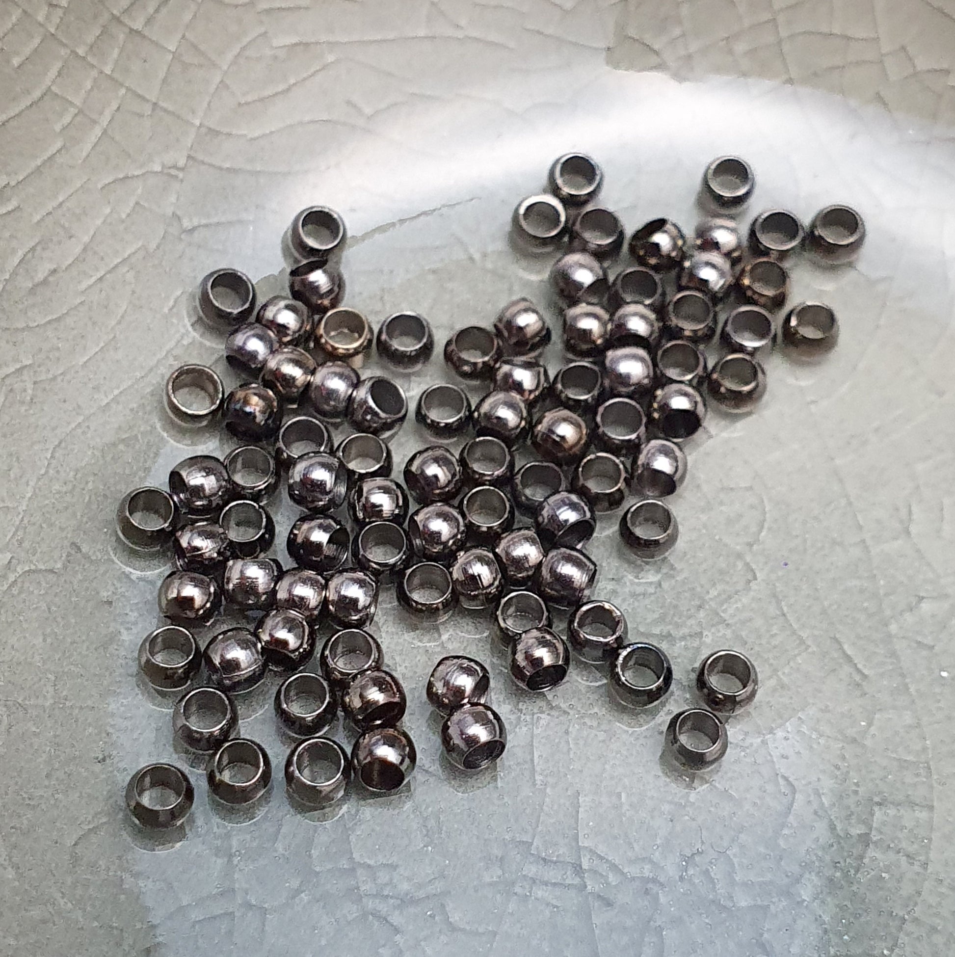 Das Bild zeigt Quetschperlen in Anthrazit (geschwärzt) in Kugelform. Sie eignen sich hervorragend zum Fixieren von Perlen oder zum Bilden von Schlaufen um Verschlüsse anzubringen.