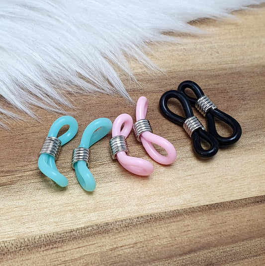 Das Bild zeigt eine Auswahl an Silikonschlaufen für Brillenketten und Maskenhalter in drei Farben: Mint, Rosa und Schwarz. Jede Schlaufe hat eine flexible, weiche Textur und ist so gestaltet, dass sie einfach auf den Bügel der Brille geschoben werden kann. An einem Ende der Schlaufe befindet sich ein kleiner Metallring, der fest angebracht ist, um ein Abrutschen zu verhindern. Die anderen Enden der Schlaufen sind offen, sodass sie mit einem Karabiner oder Biegering leicht an einer Kette befestigt werden kön