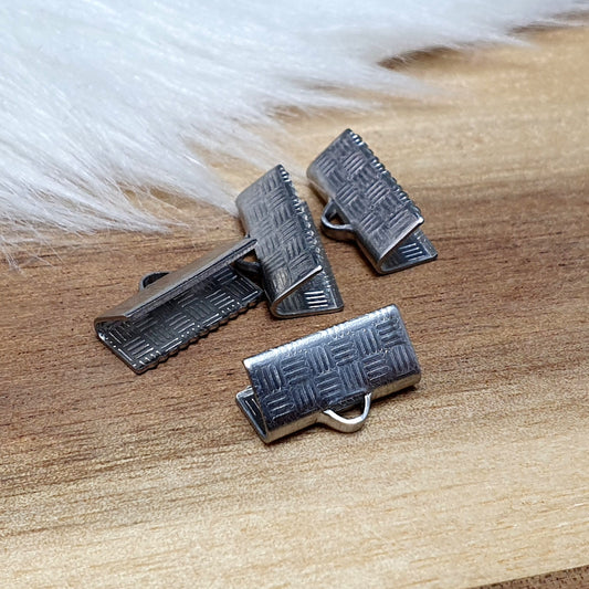 Das Bild zeigt vier Bandklemmen aus Edelstahl mit einer Breite von 13 mm. Jede Klemme ist mit speziellen "Zähnen" am unteren Backenrand ausgestattet, die ein Abrutschen der Bänder verhindern. Die Bandklemmen sind ideal für die Befestigung von Verschlüssen an Stoff- und Lederbändern und eignen sich perfekt für verschiedene Anwendungen wie Kropfbänder, Halsbänder und Armbänder. Die silberfarbene Oberfläche verleiht den Klemmen ein modernes und ansprechendes Aussehen.