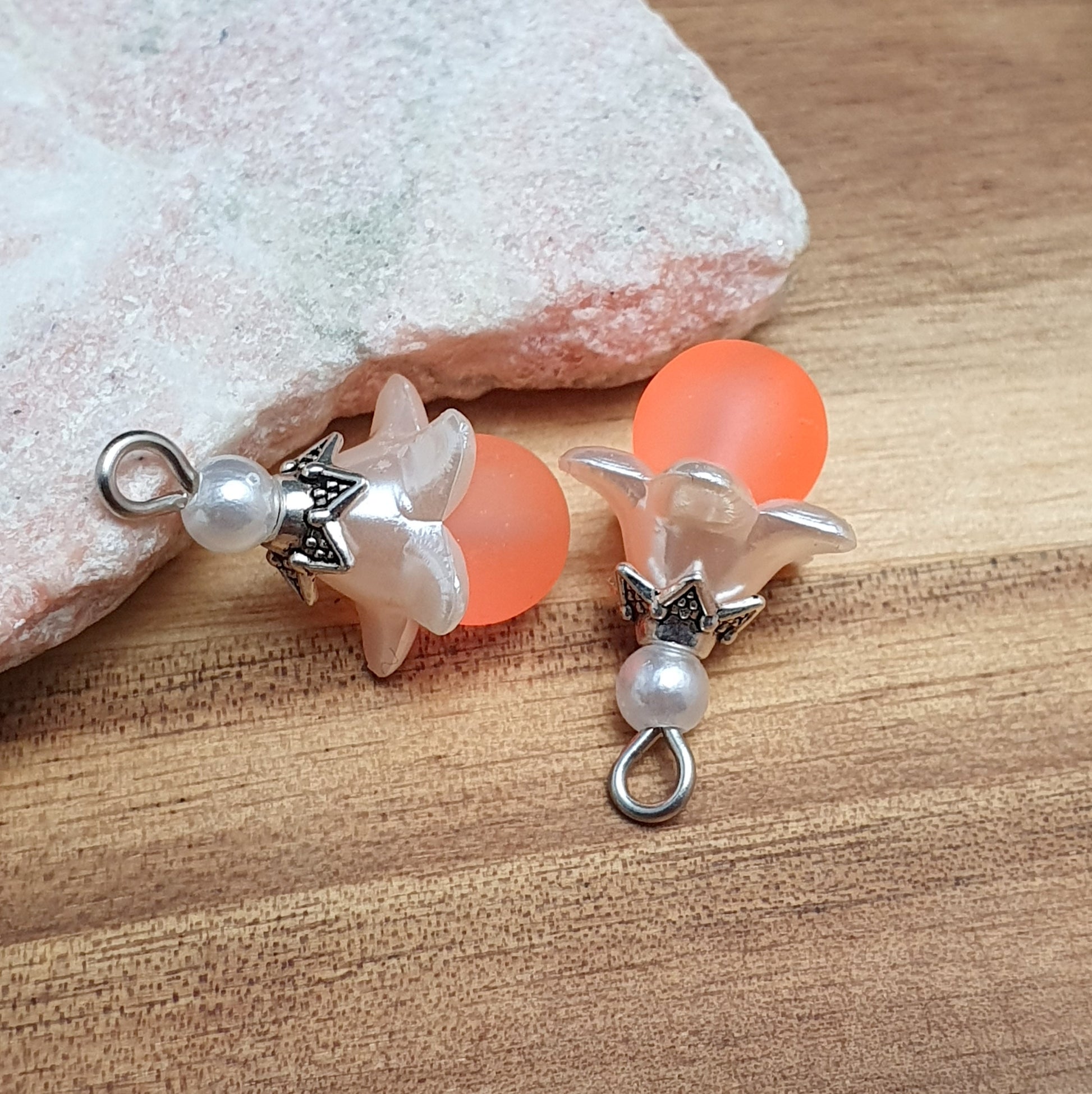 Das Bild zeigt ein 30-teiliges Bastelset zur Schmuckherstellung, ideal für kreative Bastler. In dem Set sind Materialien enthalten, um 6 Blumenanhänger in Orange und Weiß zu gestalten. Zu sehen sind verschiedene Komponenten: matte orangefarbene Glasperlen, cremeweiße Acrylperlen, weiße Blütenkäppchen und antik silberfarbige Sternkäppchen. Alle Teile sind sorgfältig angeordnet, um die Vielseitigkeit und Farbpalette des Sets hervorzuheben. Dieses Set bietet die perfekte Grundlage für die Gestaltung einzigarti