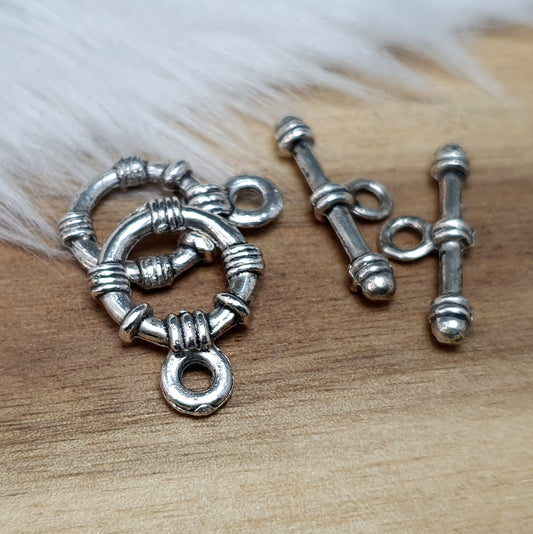 Die Abbildung zeigt zwei antik silberfarbene Knebelverschlüsse, bestehend aus einem Ring und einem Stab. Diese hochwertigen Verschlüsse bieten eine elegante Lösung für Schmuckstücke wie Armbänder und Ketten. Ihr klassisches Design verleiht jedem Projekt eine dekorative Note und sorgt gleichzeitig für eine sichere Verschlussmöglichkeit.