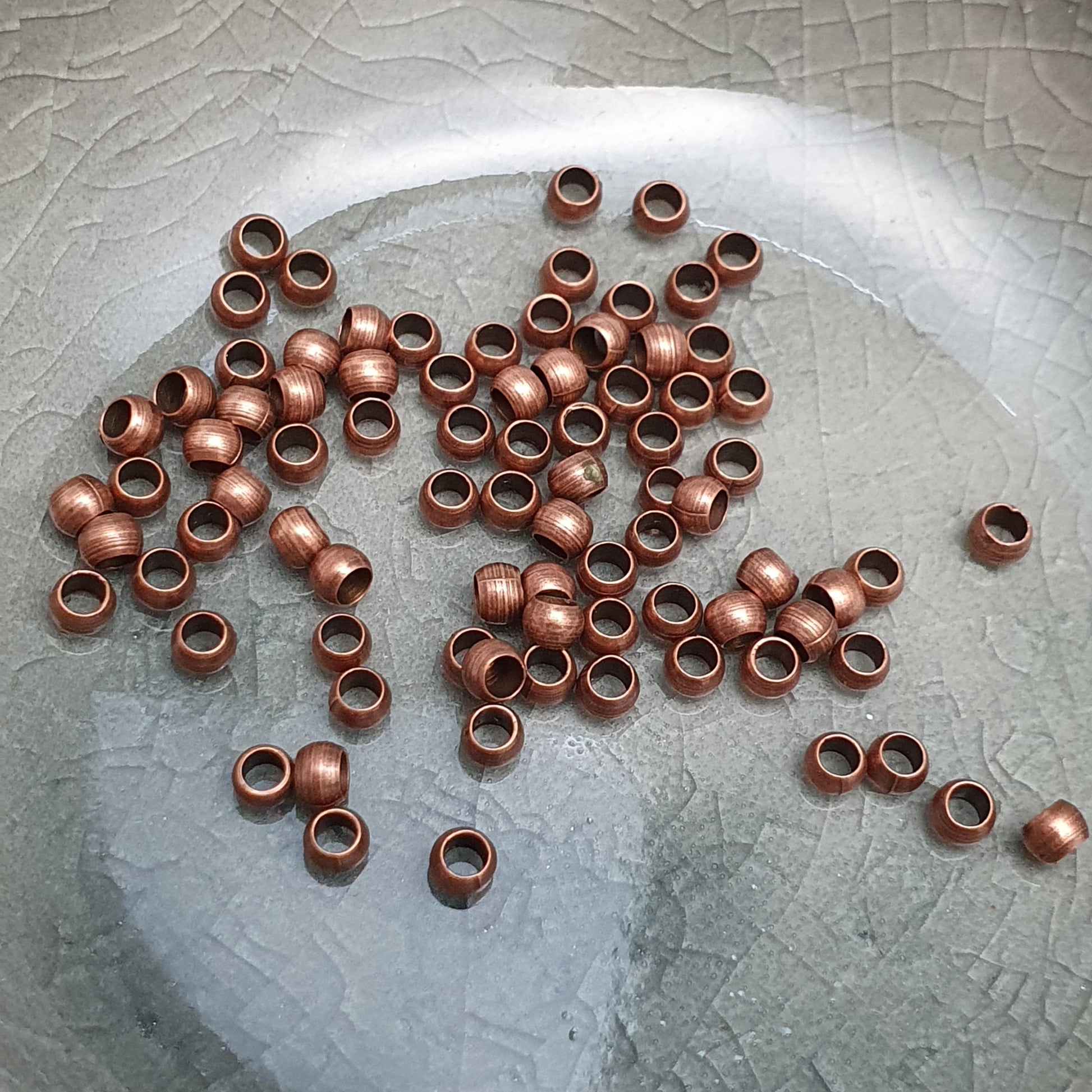 Das Bild zeigt Quetschperlen in Kugelform, antik kupferfarbig mit einem Durchmesser von 2,5mm. Ideal zum Fixieren von Perlen.