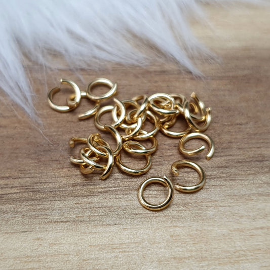 Das Bild zeigt 20 offene Biegeringe aus hochwertigem, vergoldetem Edelstahl mit einem Durchmesser von 5 mm. Die Ringe sind in einem praktischen Set angeordnet und verfügen über eine glänzende goldene Oberfläche, die dem Schmuckdesign einen eleganten Akzent verleiht. Dank des offenen Designs sind die Ringe leicht zu handhaben und ermöglichen eine einfache Verbindung von Schmuckelementen wie Anhängern oder Perlen. Diese Biegeringe sind ideal für die Herstellung individueller Schmuckstücke, darunter Armbänder,